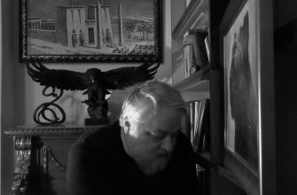 Меняйлов в чёрно-белом цвете, на заднем фоне орёл и картина с изображением древнего египетского храма